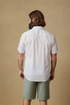 Man wearing a white shirt and green shorts against a beige background