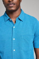 Man wearing a blue short-sleeve shirt against a gray background