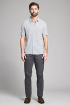 Man wearing a light gray short-sleeve shirt and dark gray pants on a plain background