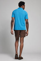 Man wearing a blue polo shirt and brown shorts on a gray background