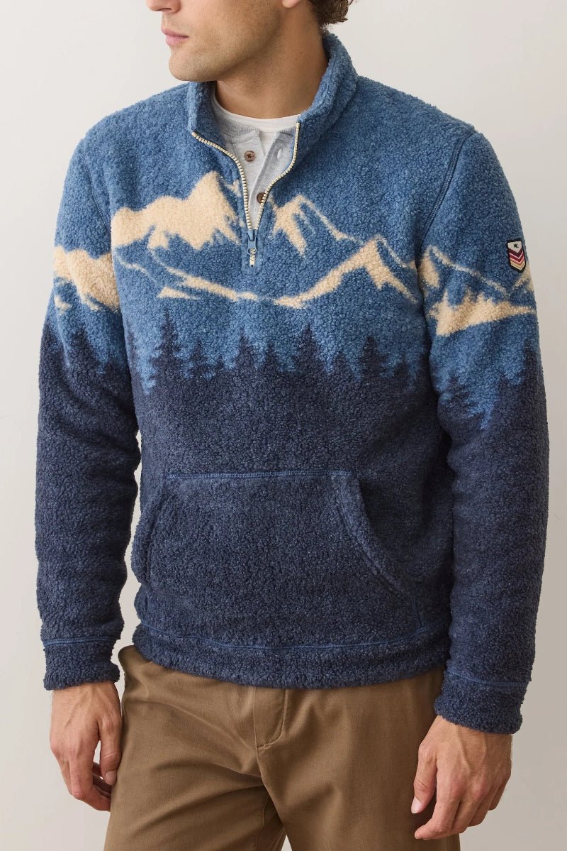 Man wearing a blue sweater with mountain and forest design against a plain background