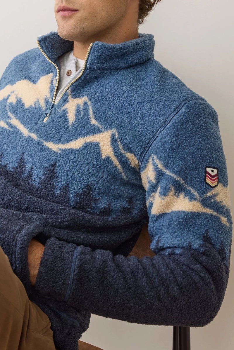 Person wearing a blue fleece pullover with a pattern, sitting against a neutral background