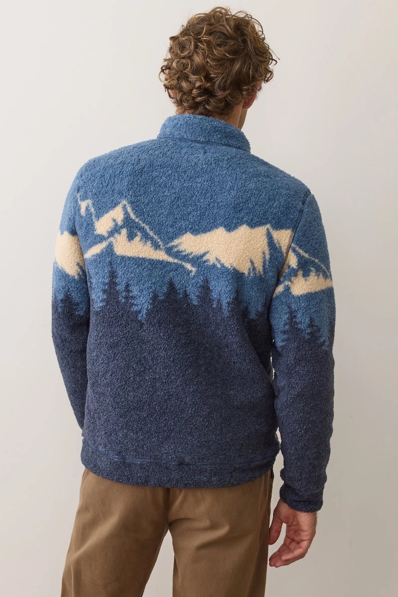 Person wearing a blue sweater with mountain design on the back against a plain background