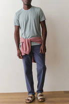 Person wearing a light blue t-shirt, pink apron, and blue pants against a plain background