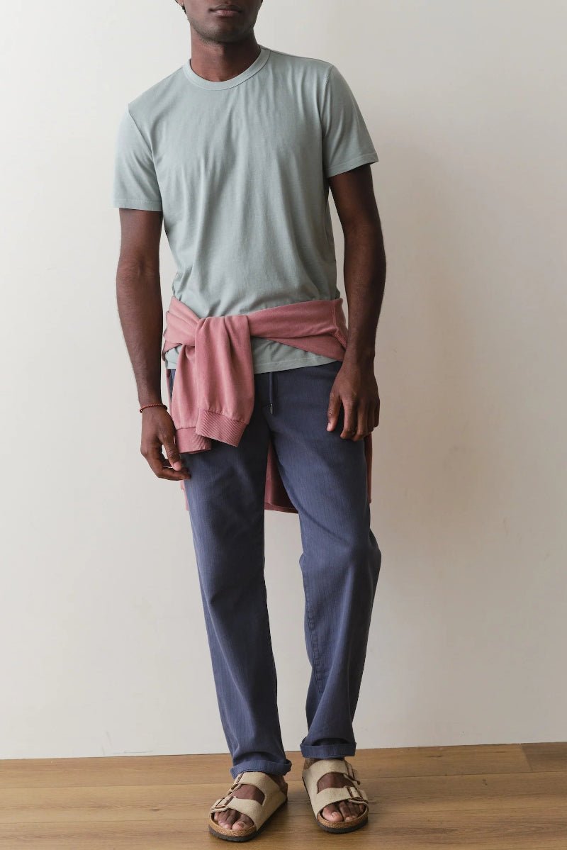 Person wearing a light blue t-shirt, pink apron, and blue pants against a plain background