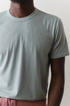 Person wearing a light gray t-shirt and pink pants against a plain background