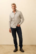 Man wearing a checkered shirt and dark jeans against a beige wall.