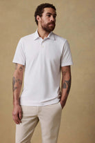 Man wearing a white polo shirt and beige pants against a beige background