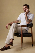 Man sitting on a chair wearing a white shirt and beige pants against a beige background