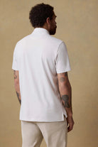 Man wearing a white polo shirt and beige pants against a beige background