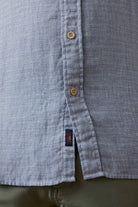 Close-up of a buttoned shirt with a brand logo on a plain background