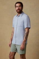 Man wearing a light blue shirt and green shorts against a beige background