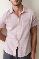 Man wearing a light pink short-sleeve shirt against a plain background