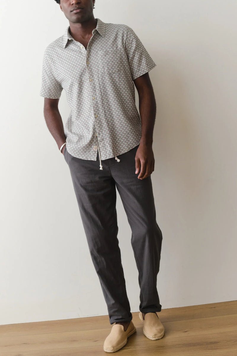 Man wearing a patterned short-sleeve shirt and dark pants against a plain background