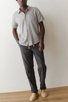 Man wearing a patterned short-sleeve shirt and dark pants against a plain background