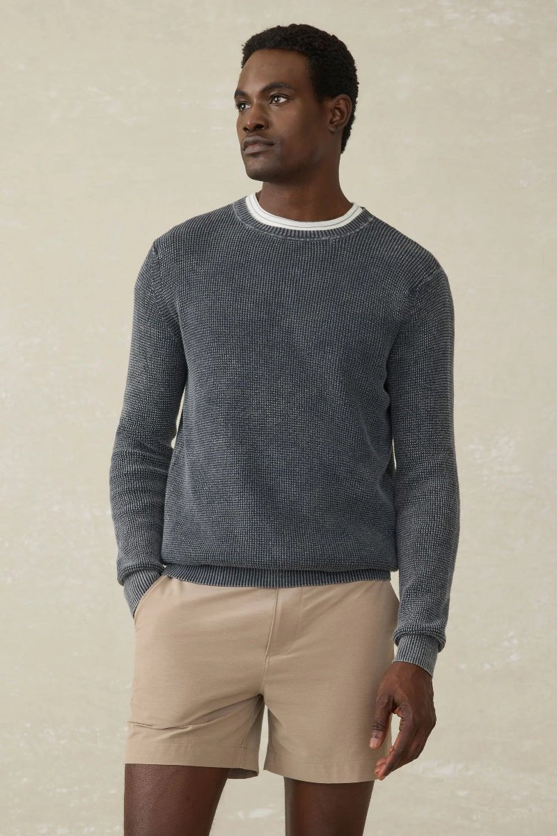 Man wearing a textured gray sweater and beige shorts against a neutral background