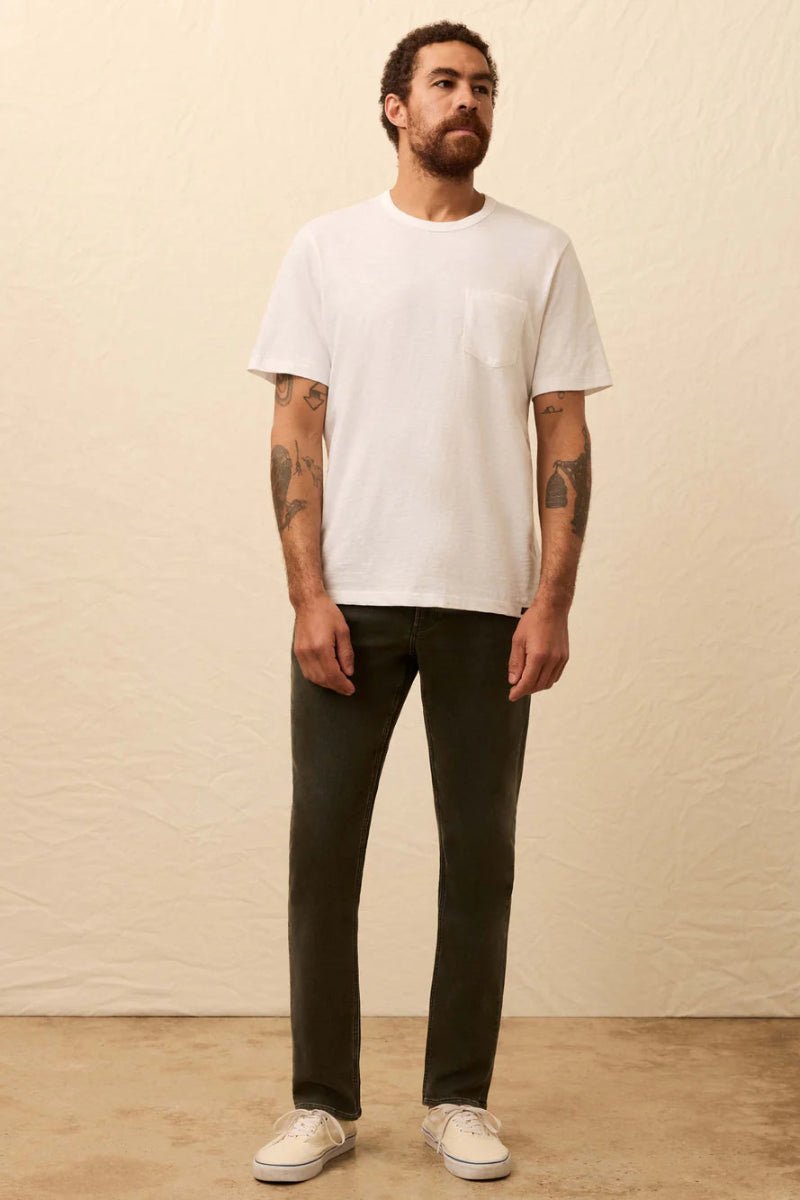 Man wearing a white t-shirt and dark pants against a beige wall.