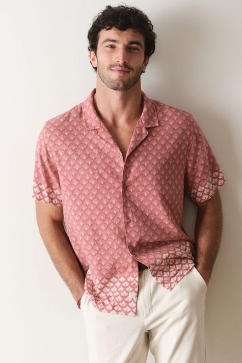 Man wearing a pink patterned shirt and white pants against a plain background