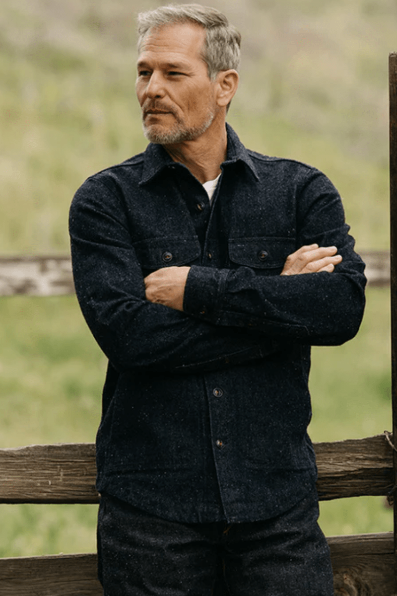 Man standing with arms crossed in a field with wooden fences.