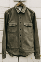 Green jacket with button details on a wooden hanger against a white wooden panel background