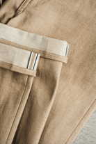 Close-up of beige pants with a pocket detail on a light gray surface