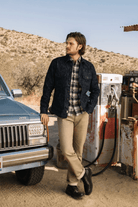 Man standing next to a vintage Jeep at a gas station with a desert landscape in the background