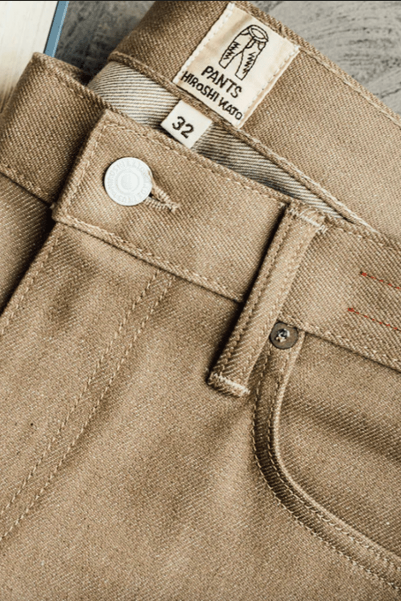 Close-up of beige pants with labels and an open book on a wooden surface