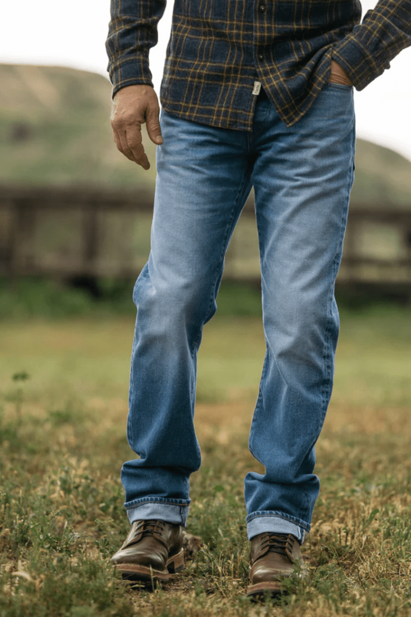 Person wearing blue jeans and a plaid shirt standing in a grassy field.
