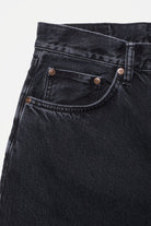 Close-up of black jeans with a brand logo on a light gray background
