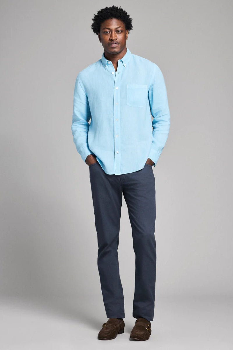 Man wearing a light blue shirt and dark pants against a plain background