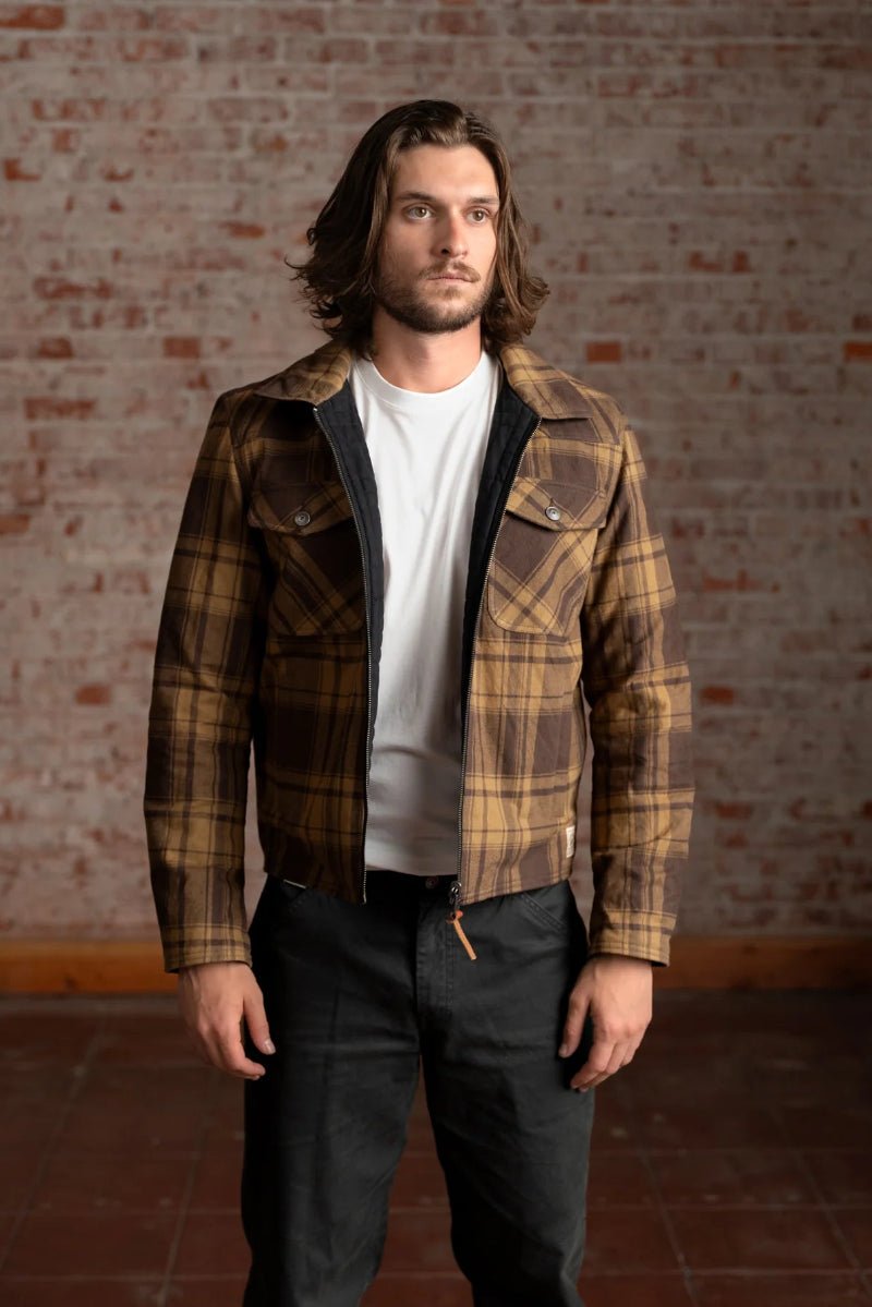 Man wearing a plaid jacket over a white shirt against a brick wall.