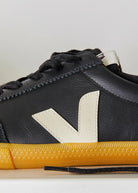 Black sneaker with yellow sole on a light gray background