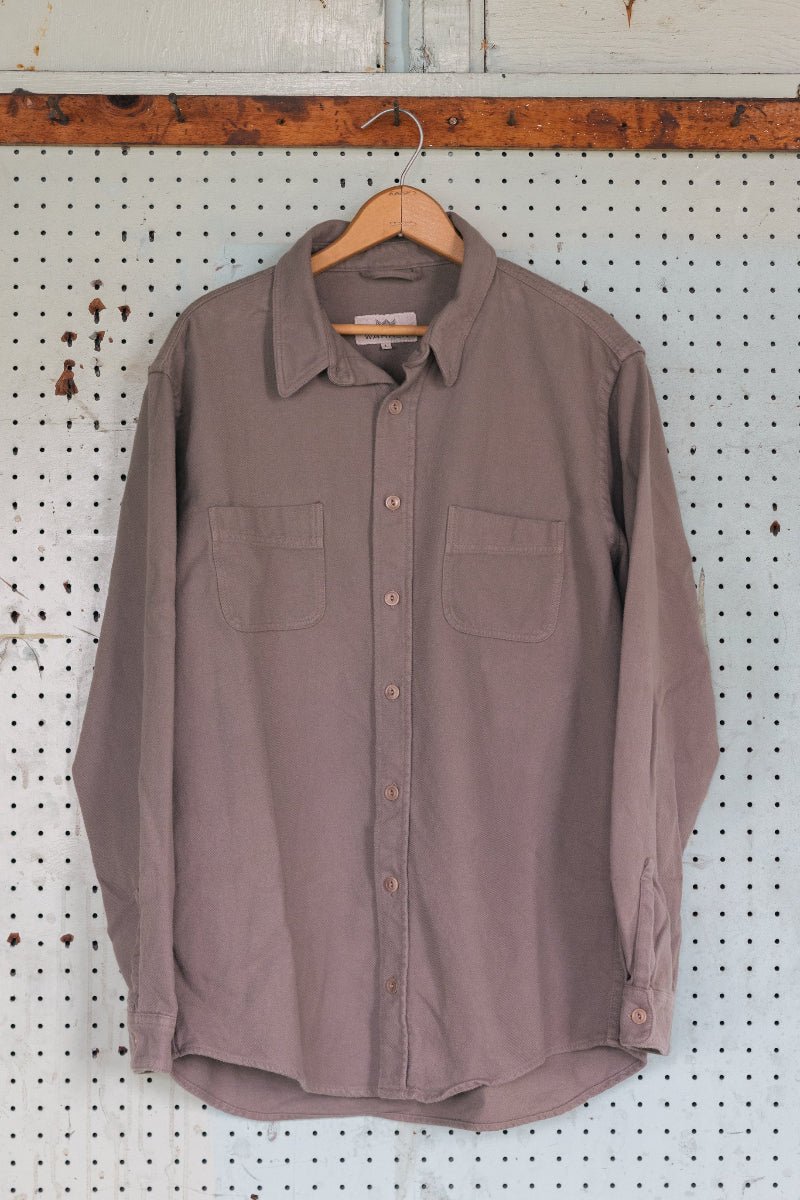 Brown button-up shirt on a hanger against a pegboard wall.