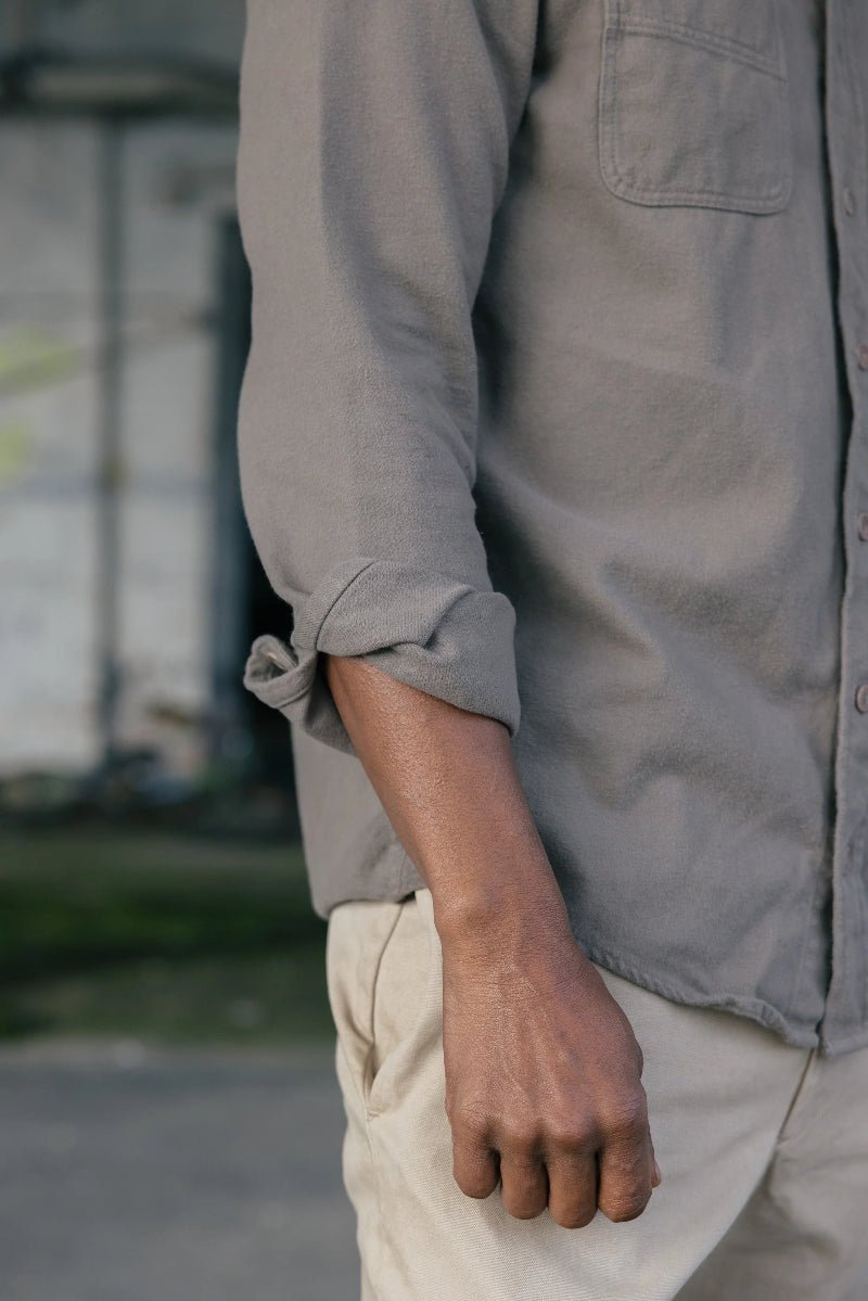 Person wearing a light gray shirt with rolled-up sleeves, standing outdoors.