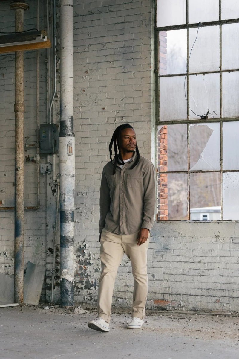 Man standing in an industrial setting with large windows and exposed brick wall.