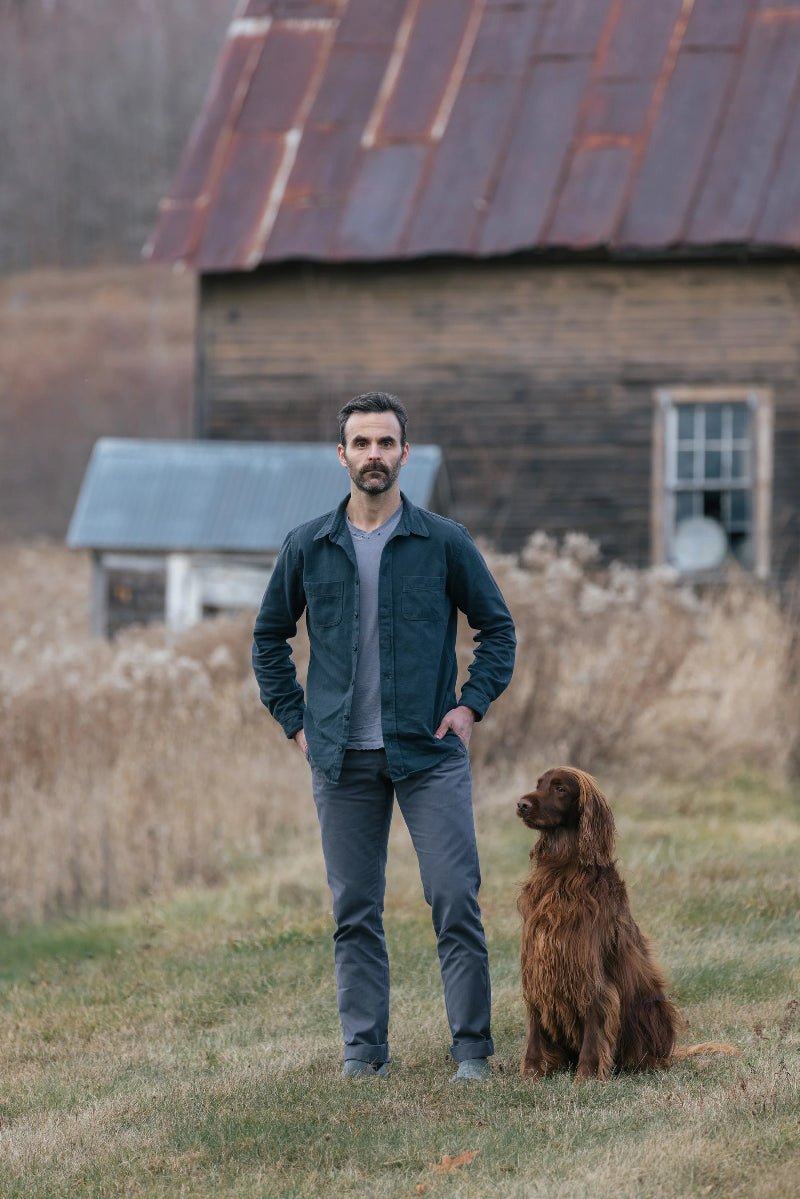 Man standing with a dog in front of an old wooden building