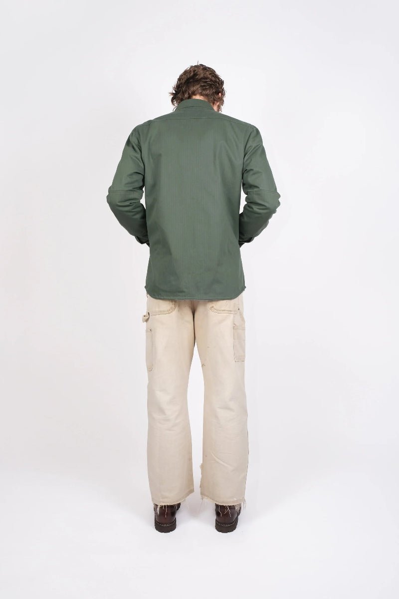 Person wearing a green jacket and beige pants on a white background