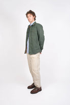 Man wearing a green jacket, light shirt, beige pants, and brown shoes on a white background