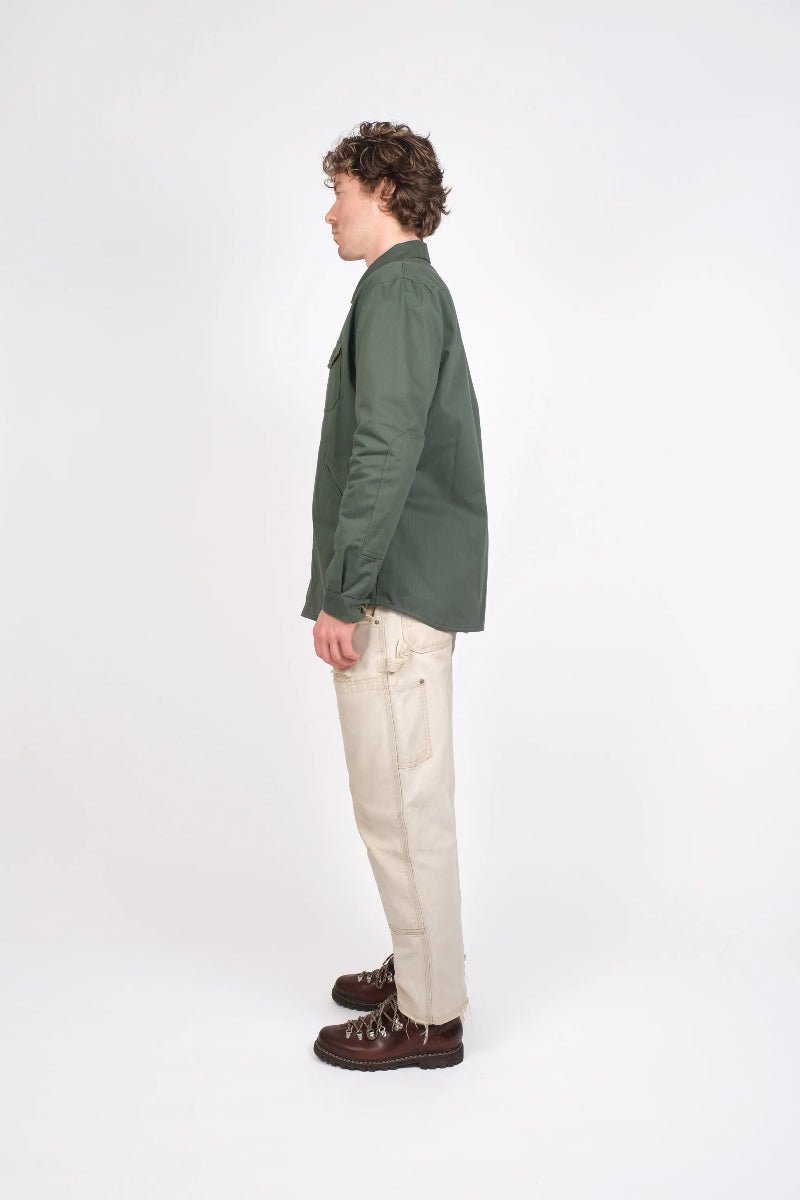 Person wearing a green jacket and beige pants standing against a white background
