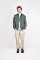 Man wearing a green jacket, light blue shirt, beige pants, and brown shoes on a white background