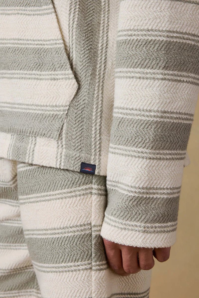 Close-up of a person wearing a patterned sweater with a visible brand logo on a beige background