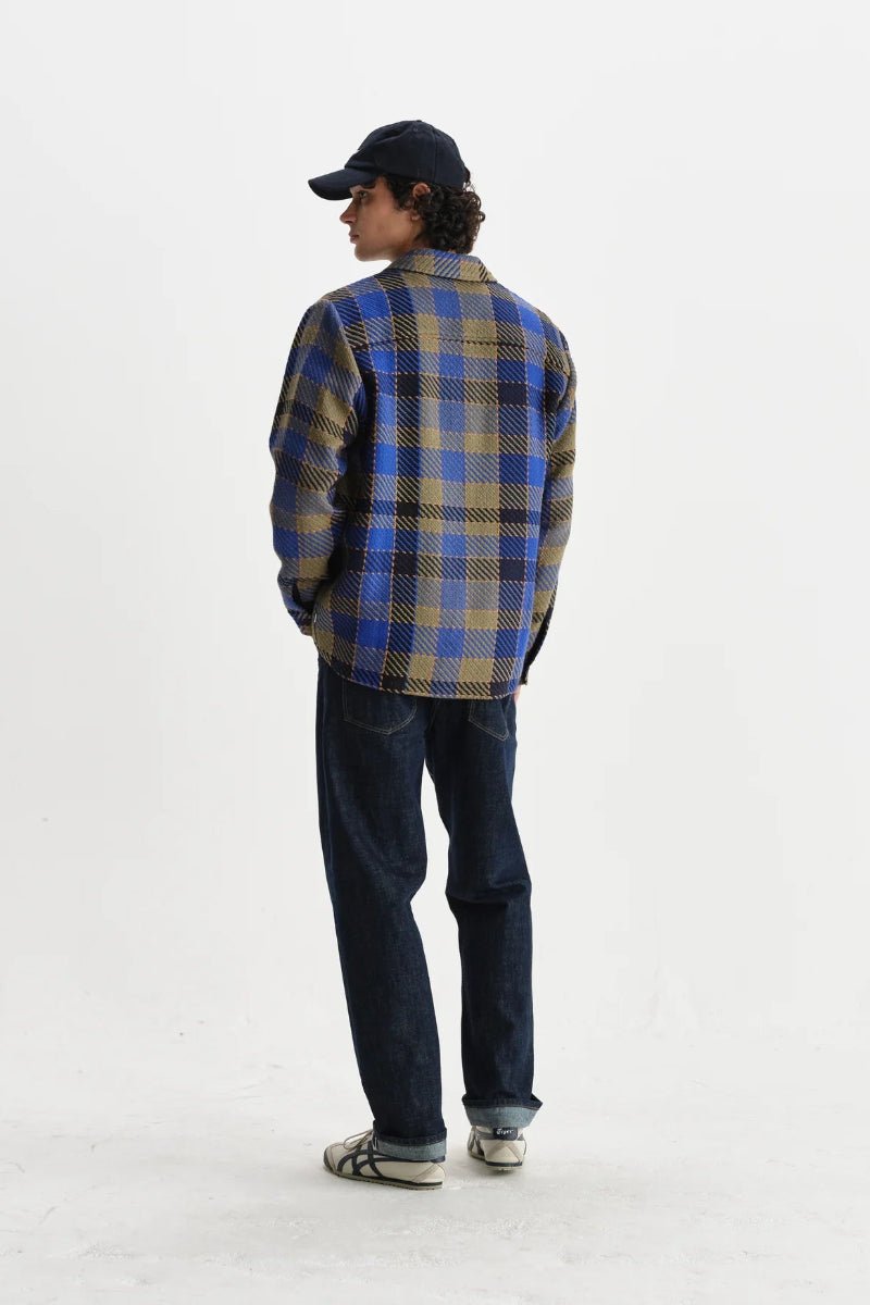 Person wearing a blue and yellow plaid shirt and dark jeans on a white background