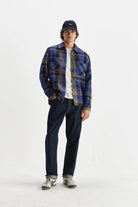 Person wearing a blue plaid shirt, dark jeans, and a cap on a white background