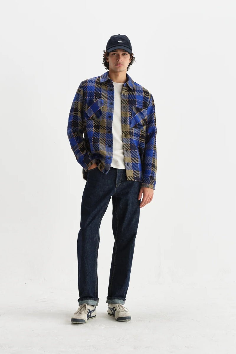 Person wearing a blue plaid shirt, dark jeans, and a cap on a white background