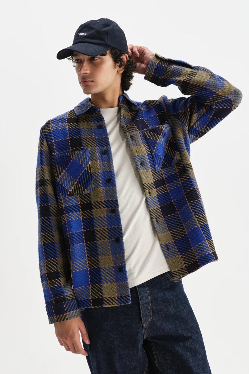 Person wearing a blue and brown plaid jacket with a white shirt underneath on a light gray background