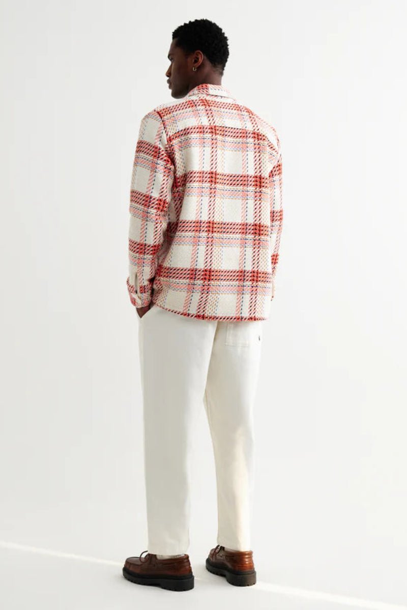 Person wearing a red and white plaid shirt with white pants on a white background