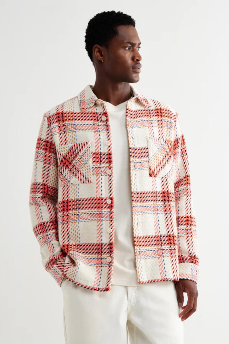 Man wearing a red and white plaid shirt over a white shirt on a light gray background